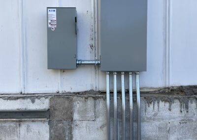 A wall-mounted electrical panel and junction box connected by conduit pipes. The panel is labeled "Eaton" and the junction box is affixed above a concrete surface.