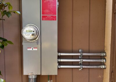 An electrical meter box with a caution sign mounted on a brown wooden wall, connected to three conduit pipes running horizontally.